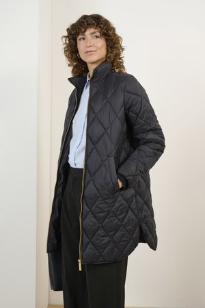 Schwarze gesteppte Pufferjacke mit hohem Kragen, goldener Reißverschluss und Seitentaschen, getragen über einem hellblau gestreiften Hemd mit glatter Textur.