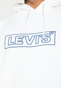 Sudadera blanca de algodón que presenta un logotipo rectangular azul de LEVI'S en la parte frontal, con cordones en el escote.