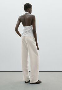 White halter top with a raw edge, paired with loose, cream-colored pants. The fabric appears soft and lightweight. Flat sandals complete the look.