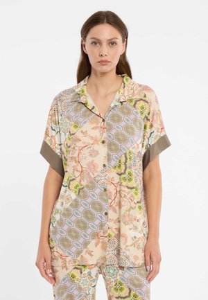 Woman wearing pastel-colored, floral and geometric patterned short-sleeve button shirt and matching pants against plain background.
