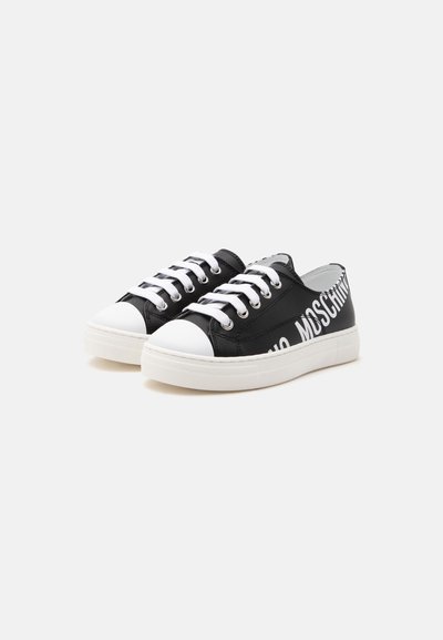 Baskets basses noires avec lacets et semelles blancs, embouts blancs et grand logo blanc « MOSCHINO » sur le côté.