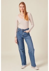 Helle beige gerippte Langarmbluse mit Knöpfen und blauen hochgeschnittenen Jeans aus Denim. Die Jeans haben einen lockeren Schnitt und sind leicht abgewetzt.