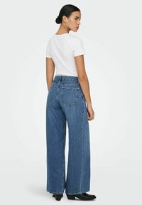 Jean bleu taille haute à jambes larges en denim, doté de deux poches arrière et d'une coupe classique. Associé à un t-shirt blanc ajusté.