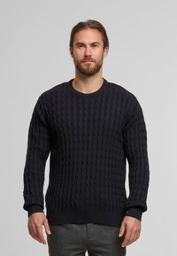 Maglione cable-knit di un blu navy scuro con colletto rotondo, caratterizzato da una texture a coste e maniche lunghe. Realizzato in una morbida miscela di lana, indossato da un modello.