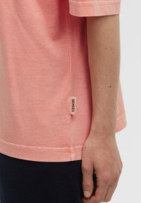 Helles rosa T-Shirt aus weichem Stoff, mit einem Seitennahtetikett, auf dem "SENSES" steht, in lockerer Passform und mit kurzen Ärmeln.