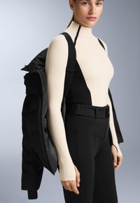 Pruhovaný rolák v krémové a černé barvě s dlouhými rukávy, spárovaný s těsnými černými kalhotami a rozepnutou černou bundou, kterou má přehozenou přes rameno.