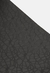 Musta tekstuuripintainen materiaali, jossa on matomaista kuviota. "Casual" on kohotettu pinnalle, mikä lisää ulottuvuutta ilman värieroa.