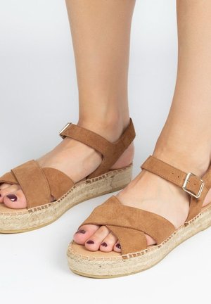 Bruine suède espadrille sandalen met gekruiste banden, enkelgesp en een geweven jute zool. Open-toe ontwerp onthult geschilderde teennagels.
