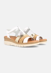 Sandalias blancas y doradas para mujeres con tiras entrecruzadas, una plantilla acolchada y una suela de cuña ligera en color beige.