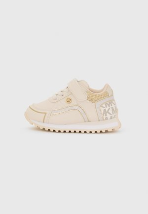 Zapatillas infantiles beige con una tira de velcro, paneles de malla texturizada y detalles en dorado. Presenta una suela de goma estriada y un logo en el lateral.