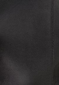 Surface en cuir texturé noir avec une couture verticale sur le côté droit.
