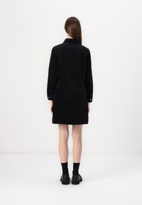 Black corduroy shirt dress with long sleeves, button cuffs, and a straight cut. Simple design and smooth texture, reaching mid-thigh.