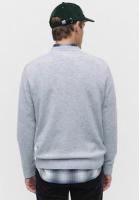 Grå stickad tröja med ribbade ärmslut, bärs över en blå och vit rutigt skjorta, med en grön kordflorsmössa. Bakifrån.