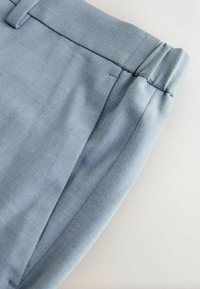 Gros plan sur un tissu bleu clair d'un pantalon, montrant la poche et la taille élastique avec les détails de texture et de couture.