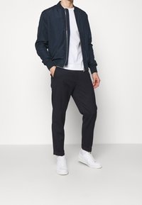 Námořnicky modrá bomber bunda s stojáčkovým límcem, bílým tričkem s kulatým výstřihem, tmavé kalhoty a bílé tenisky, zdůrazněné čistými liniemi a přiléhavým střihem.