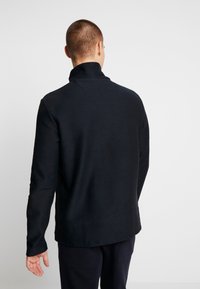 Granatowy sweter z wysokim kołnierzem, teksturowana tkanina, długie rękawy i luźny krój. Prosty design bez widocznych logo czy wzorów.