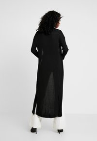 Lång svart ribbad cardigan med en lös passform, med sidofickor och långa ärmar. Tillverkad av lätt, texturerat tyg.