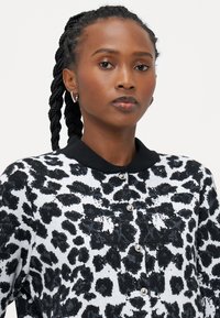 Czarny i biały kardigan w panterkę z czarnym kołnierzem, z zapięciem na guziki i teksturowanym materiałem.