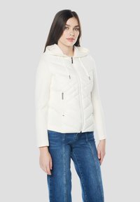 Fehér kapucnis pulóver steppelt mintával, cipzáras záródással és két oldalzsebbel. Sima textúra, laza fazon, bordázott ujjakkal.