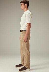 Beige chino's en een witte t-shirt met korte mouwen. Donkerbruine riem en sneakers. De pasvorm is ontspannen, met een soepele textuur op de stof.