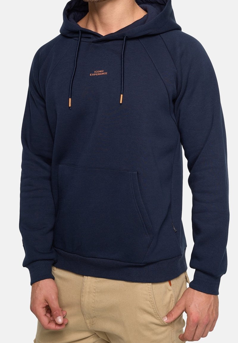 Marineblå hættetrøje med en frontlomme, snor i hætten, et lille logo på brystet og ribbet manchetter og kant. Materiale af bomuldsblanding; glat tekstur.