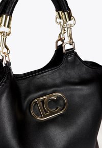 Černá kožená kabelka s výrazným zlatým logem a pevným madlem, která ukazuje elegantní a moderní designové prvky.