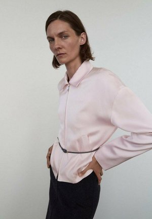 Veste en satin rose clair avec fermeture éclair, col pointu, manches longues et taille cintrée. Dotée de poches latérales et d'une texture lisse.