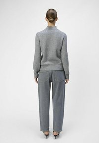 Suéter de punto gris con un patrón texturizado, dobladillo y puños acanalados; combinado con jeans de denim de corte suelto y alta cintura en un lavado gris claro.