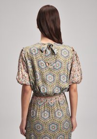 Set di blusa a maniche corte e gonna in tessuto stampato. Presenta maniche a palloncino, lacci sul retro, con motivi geometrici e floreali in verde e rosa.