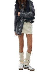 Svartrandig pufferväst över en grå rutig skjorta, lager över en krämfärgad minisk skirt. Ribbade krämfärgade benvärmare och vita sneakers med gråa accenter.