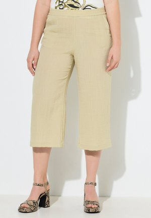 Beige, weit geschnittene, gekürzte Hose, getragen von einer Person, kombiniert mit hochhackigen Sandalen aus Schlangenleder und einem gemusterten Oberteil.