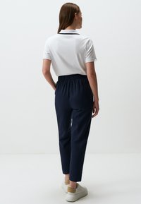 Marineblauwe broek met elastische taille en taps toelopende benen, gecombineerd met een wit poloshirt. Glad materiaal, eenvoudig ontwerp en casual schoenen.