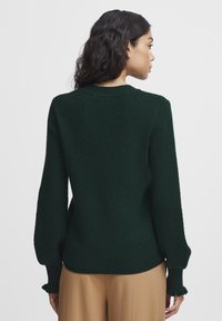 Dark green textured knit sweater with a round neckline and long sleeves, featuring ruffled cuffs and a relaxed fit.