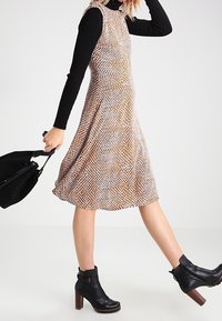 Polvipituinen A-linjainen mekko, jossa on teksturoitu, kuvioitu kangas maanläheisissä sävyissä. Musta pitkähihaisuus ylle, yhdistettynä nilkkatakkiin.