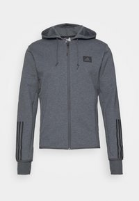 Grauer Kapuzenpullover mit Reißverschluss, verstellbarer Kapuze, strukturiertem Stoff, schwarzem Adidas-Logo auf der Brust und drei schwarzen Streifen an jedem Ärmel.