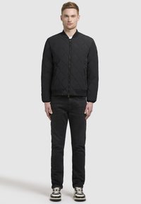 Svart quiltad bomberjacka med en enfärgad design, ribbade manschetter och två sidofickor, ihop med mörka jeans och sneakers.