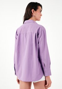 Purple long-sleeve shirt with a classic collar, buttoned cuffs, and a relaxed fit. Smooth cotton fabric with a slightly shiny finish.