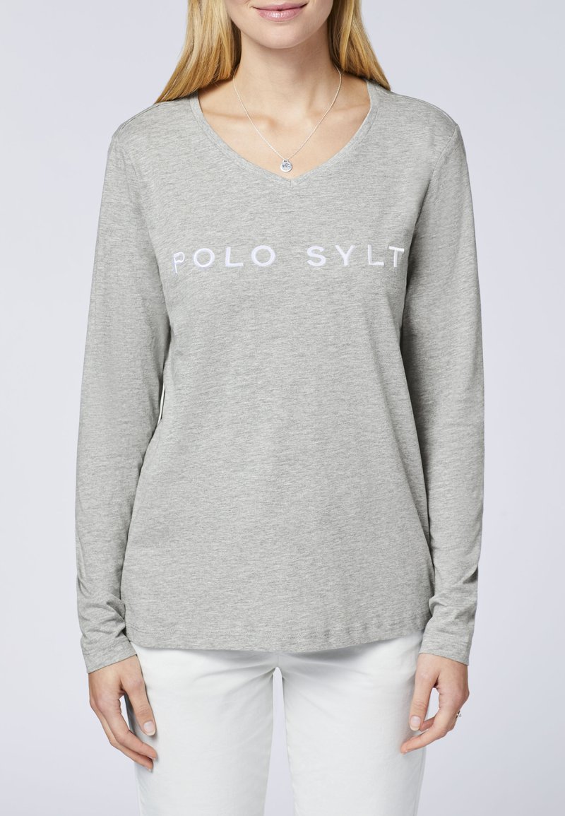 Graues Langarm-T-Shirt mit V-Ausschnitt und weißem "POLO SYLT"-Schriftzug über der Brust. Weiches Material; figurbetontes Design; kombiniert mit weißen Hosen.