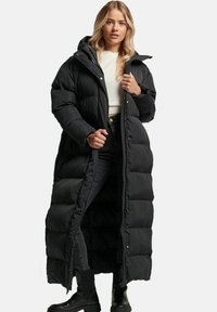 Sort lang dunjakke med hætte, der har et quiltet design, frontlukning med trykknapper, sidelommer og en elegant, glat tekstur.