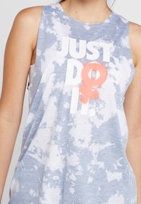 Débardeur sans manches en tie-dye bleu clair, arborant un texte blanc audacieux "JUST DO IT." avec un accent en forme de symbole féminin rose. Texture de tissu douce.