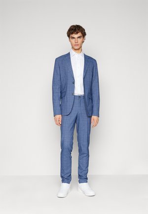 Lichtblauw geruit pak met een gestructureerde blazer en op maat gemaakte broek, gecombineerd met een wit overhemd en witte sneakers. Gladde textuur.