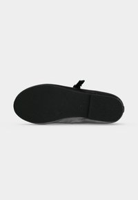 Semelle de chaussure noire avec grip texturé, talon plat et un petit logo circulaire près du centre.