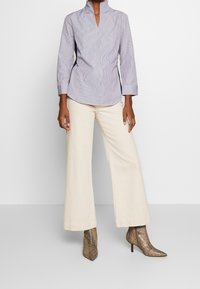 Randig skjorta i ljusblått och vitt, ihop med vida krämfärgade byxor och bruna stövletter i ormskinnsmönster.