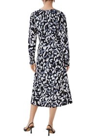 Langärmliges Kleid mit einem schwarz-weißen abstrakten Muster und blauen Akzenten, das einen gerafften Ausschnitt und einen mittellangen Saum aufweist.