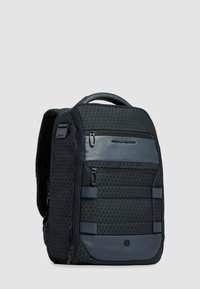 Zaino con motivo geometrico nero e blu scuro, con molteplici tasche con cerniera e maniglia superiore, in piedi su uno sfondo grigio.