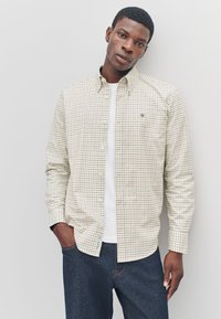 Checkered button-up shirt in cream with brown and navy squares, paired with a white t-shirt and dark jeans. Features a classic collar.