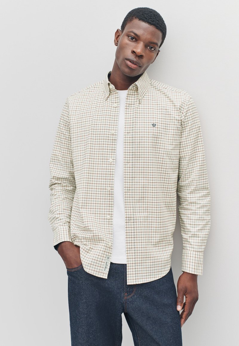 Checkered button-up shirt in cream with brown and navy squares, paired with a white t-shirt and dark jeans. Features a classic collar.