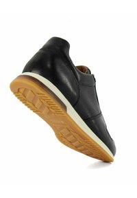 Chaussure en cuir noir avec une tige texturée, doublure en cuir beige et semelle en caoutchouc présentant un motif en nid d'abeille. Semelle intermédiaire blanche avec des accents de couleur contrastés.