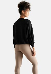 Sweatshirt noir surdimensionné avec des épaules tombantes, associé à des leggings beige clair. Le tissu semble doux, avec des poignets côtelés et une texture lisse.