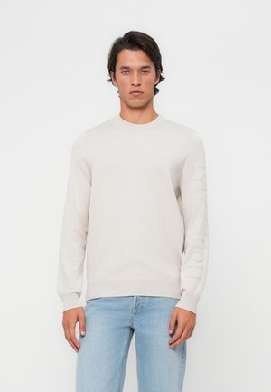 Light gray knit sweater with a crew neck and long sleeves. Features tonal logo along the left sleeve. Soft texture and simple design.
